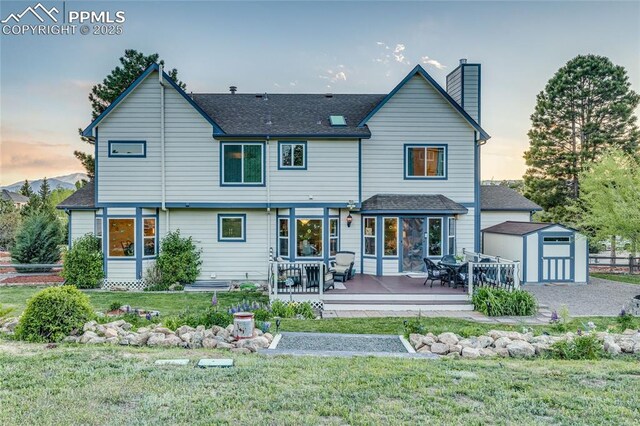 14915 Gleneagle Dr, Colorado Springs, CO 80921 - back of house at dusk with a chimney, outdoor dining area, a lawn, a shingled roof, and a wooden deck