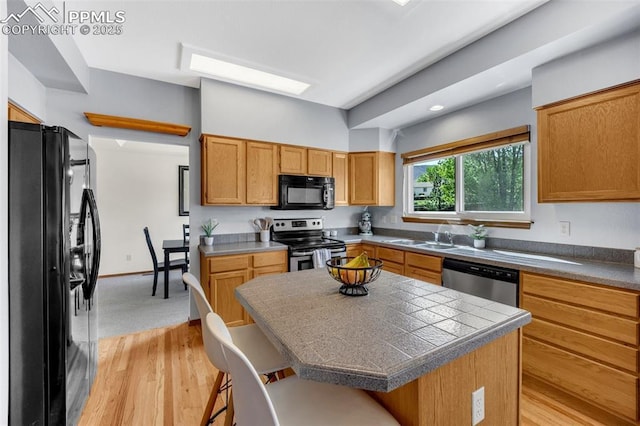 6390 Moccasin Pass Ct, Colorado Springs, CO 80919 - kitchen with black appliances, a sink, a kitchen bar, light wood finished floors, and a center island