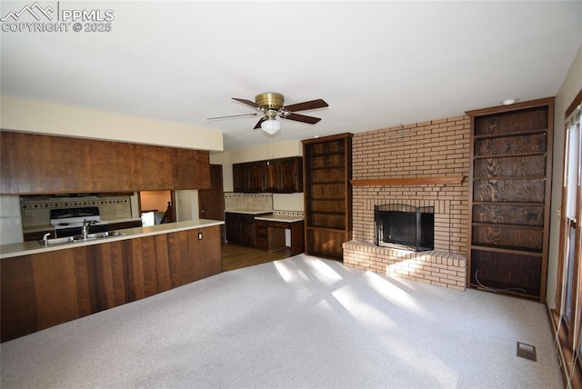 kitchen featuring a ceiling fan, carpet, light countertops, a sink, and a brick fireplace