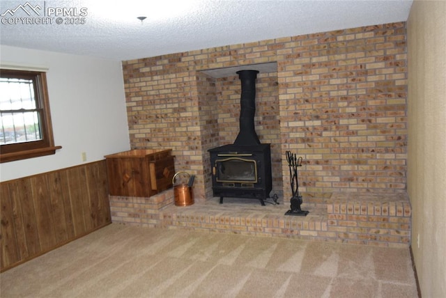 detailed view of a wood stove, wooden walls, carpet flooring, a textured ceiling, and a wainscoted wall