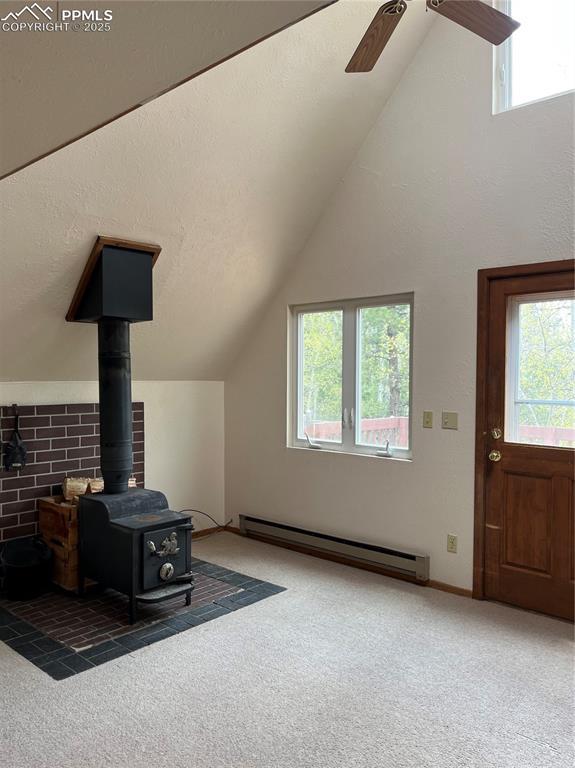 646 Grey Eagle Dr, Cripple Creek, CO 80813 - unfurnished living room featuring a wood stove, carpet, a baseboard radiator, vaulted ceiling, and ceiling fan
