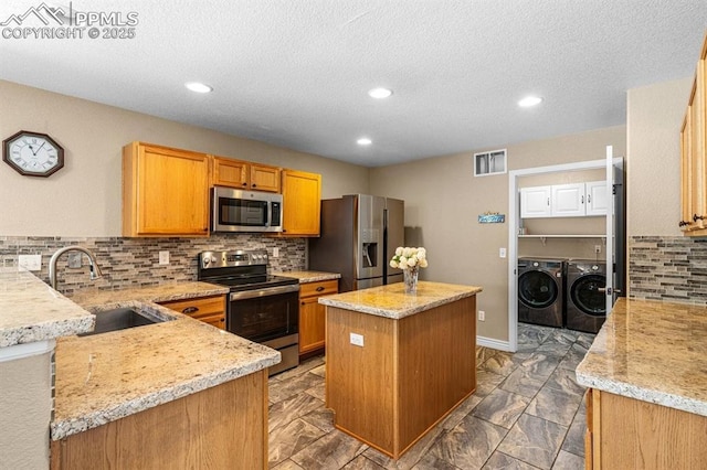 8020 Firecracker Trl, Fountain, CO 80817 - kitchen featuring appliances with stainless steel finishes, washing machine and clothes dryer, a sink, a center island, and tasteful backsplash