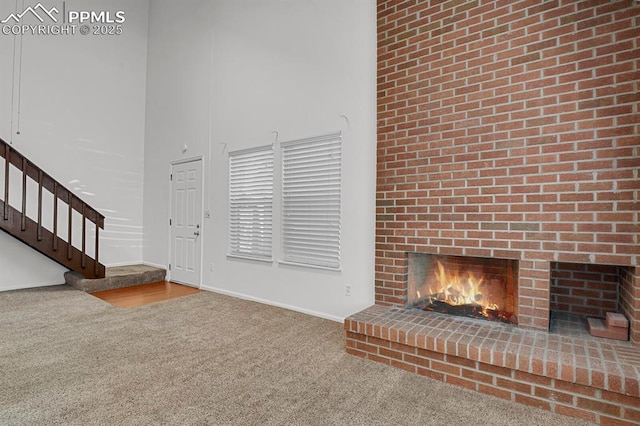 3300 W Florida Ave Unit 26, Denver, CO 80219 - unfurnished living room with carpet, stairs, a high ceiling, a brick fireplace, and baseboards