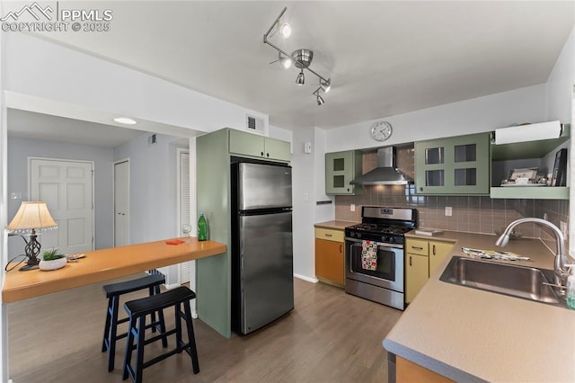 2321 N Meade Ave, Colorado Springs, CO 80907 - kitchen with stainless steel appliances, wall chimney range hood, green cabinetry, a sink, and decorative backsplash