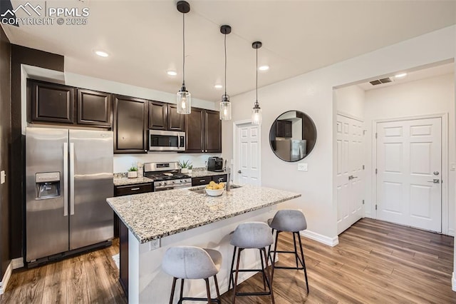 1747 Satin Spar Pt, Colorado Springs, CO 80908 - kitchen with stainless steel appliances, light wood-style floors, a breakfast bar, light stone counters, and dark brown cabinets