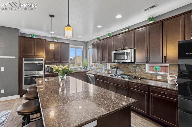 7656 Peachleaf Dr, Colorado Springs, CO 80925 - kitchen featuring appliances with stainless steel finishes, tasteful backsplash, dark stone counters, dark brown cabinets, and recessed lighting