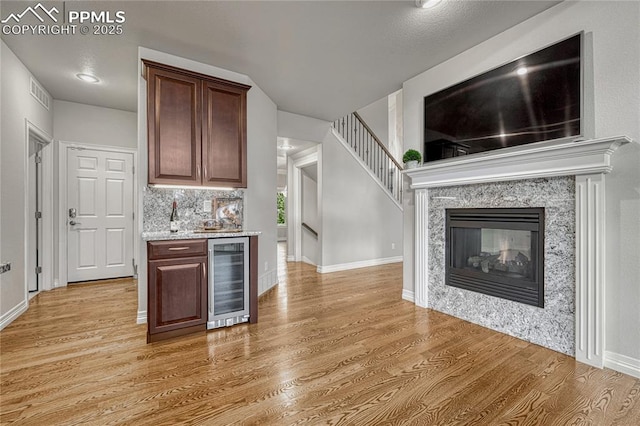 14745 Millhaven Pl, Colorado Springs, CO 80908 - indoor wet bar featuring wine cooler, light wood finished floors, a high end fireplace, baseboards, and decorative backsplash