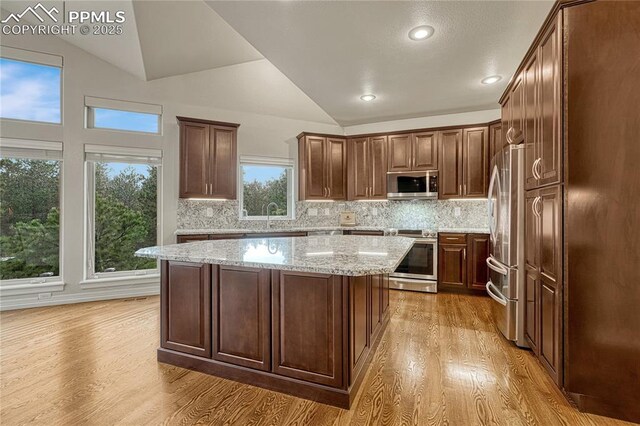14745 Millhaven Pl, Colorado Springs, CO 80908 - kitchen featuring appliances with stainless steel finishes, light wood-style flooring, vaulted ceiling, a kitchen island, and backsplash