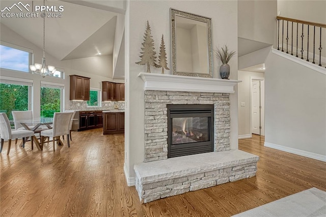 14745 Millhaven Pl, Colorado Springs, CO 80908 - living area with high vaulted ceiling, a chandelier, wood finished floors, a stone fireplace, and baseboards