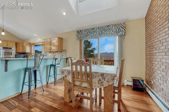 17580 Chipped Arrow Way, Monument, CO 80132 - dining space featuring light wood-style flooring, brick wall, vaulted ceiling, a baseboard heating unit, and healthy amount of natural light