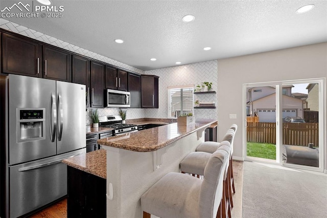7856 Calabash Rd, Colorado Springs, CO 80908 - kitchen featuring stainless steel appliances, dark stone countertops, a breakfast bar area, recessed lighting, and open shelves