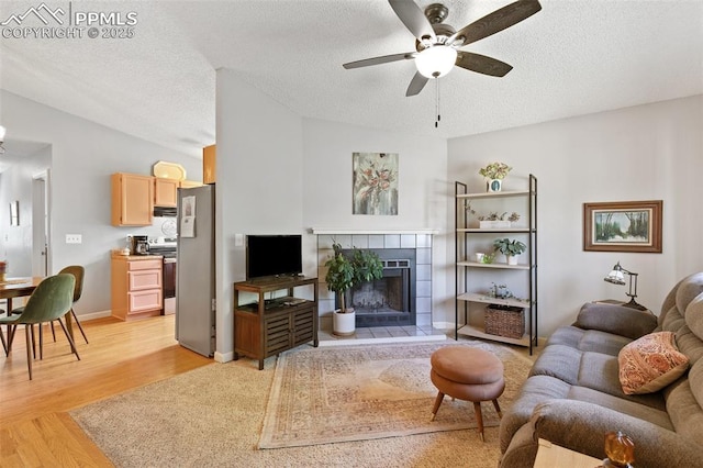 3870 Chinawood Ct, Colorado Springs, CO 80918 - living room featuring a ceiling fan, light wood finished floors, a textured ceiling, a tiled fireplace, and baseboards
