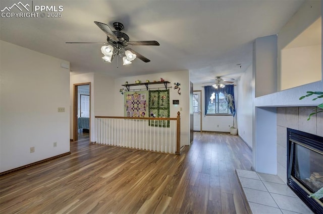 6938 Big Timber Dr, Colorado Springs, CO 80923 - unfurnished living room with ceiling fan, wood finished floors, a tiled fireplace, and baseboards