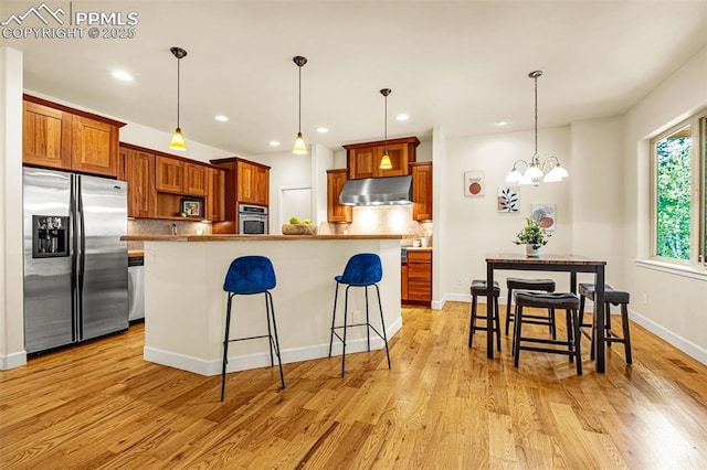 4775 Neeper Valley Rd, Manitou Springs, CO 80829 - kitchen featuring appliances with stainless steel finishes, under cabinet range hood, tasteful backsplash, a breakfast bar area, and light wood-style flooring