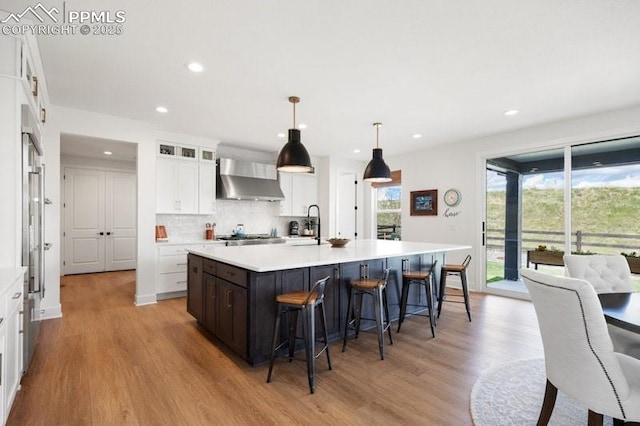 455 Rogers Way, Castle Rock, CO 80104 - kitchen featuring wall chimney exhaust hood, light wood-style floors, a breakfast bar, white cabinetry, and light countertops