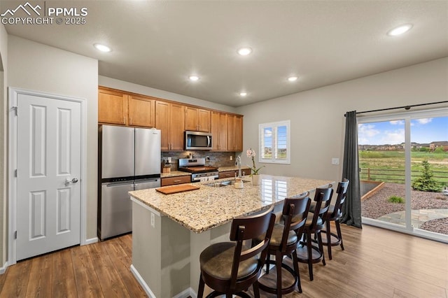10552 Summer Ridge Dr, Peyton, CO 80831 - kitchen featuring stainless steel appliances, wood finished floors, a sink, a center island with sink, and backsplash
