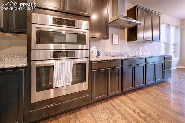4228 Notch Trl, Colorado Springs, CO 80924 - kitchen with double oven, wall chimney range hood, light wood-style floors, black electric stovetop, and dark brown cabinets