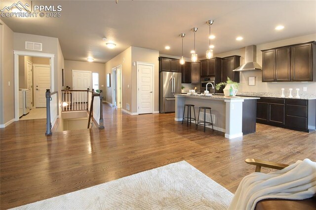 4228 Notch Trl, Colorado Springs, CO 80924 - kitchen featuring wall chimney range hood, appliances with stainless steel finishes, a breakfast bar, dark brown cabinets, and a kitchen island with sink