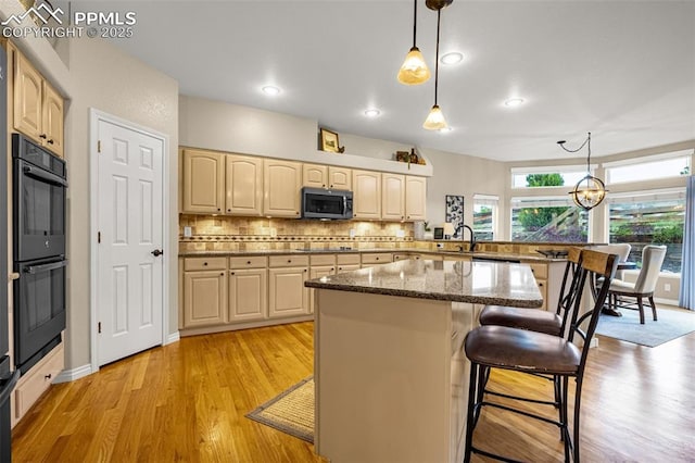 12265 Jones Park Ct, Colorado Springs, CO 80921 - kitchen with black appliances, a breakfast bar area, light wood-style floors, a sink, and pendant lighting