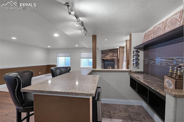 8795 Canary Cir, Colorado Springs, CO 80908 - kitchen with a stone fireplace, baseboards, a textured ceiling, light stone counters, and a kitchen bar