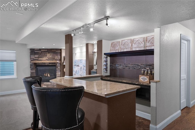 8795 Canary Cir, Colorado Springs, CO 80908 - kitchen featuring baseboards, a stone fireplace, light stone countertops, track lighting, and a textured ceiling