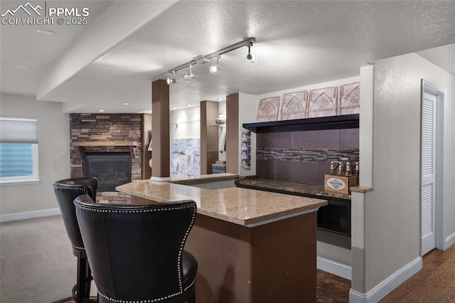 8795 Canary Cir, Colorado Springs, CO 80908 - kitchen with baseboards, light stone countertops, a stone fireplace, backsplash, and a textured ceiling