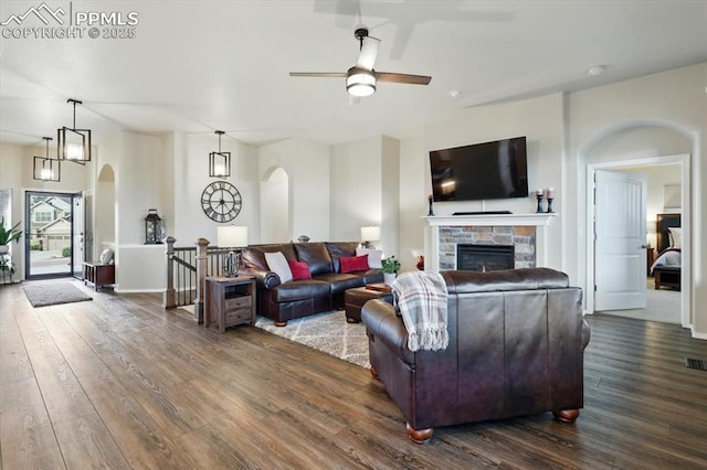 15506 Short Line Ct, Monument, CO 80132 - living area featuring arched walkways, dark wood-type flooring, a ceiling fan, a stone fireplace, and baseboards