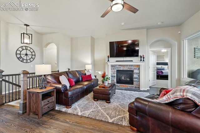 15506 Short Line Ct, Monument, CO 80132 - living room featuring arched walkways, dark wood-type flooring, a ceiling fan, and a stone fireplace