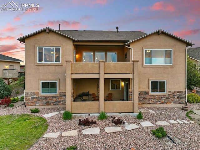 15506 Short Line Ct, Monument, CO 80132 - back of house at dusk featuring a balcony, stucco siding, stone siding, and a patio area