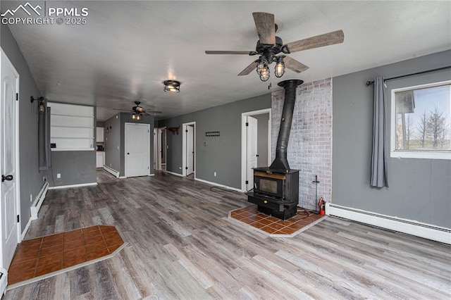 9940 N Calhan Hwy, Calhan, CO 80808 - unfurnished living room featuring a ceiling fan, a wood stove, wood finished floors, and a baseboard heating unit