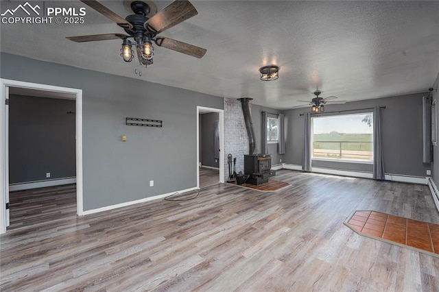 9940 N Calhan Hwy, Calhan, CO 80808 - unfurnished living room with ceiling fan, a wood stove, wood finished floors, baseboards, and baseboard heating