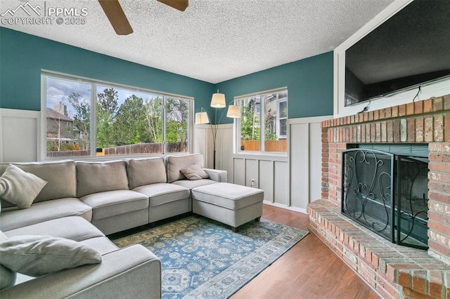 7942 French Rd, Colorado Springs, CO 80920 - living area featuring a fireplace, a wainscoted wall, ceiling fan, wood finished floors, and a textured ceiling