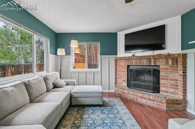 7942 French Rd, Colorado Springs, CO 80920 - living room with wood finished floors, a wainscoted wall, a textured ceiling, a brick fireplace, and a decorative wall