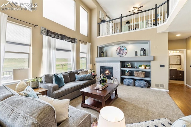 6950 Blue Mesa Ln, Littleton, CO 80125 - carpeted living room with ceiling fan, a glass covered fireplace, a towering ceiling, baseboards, and wood finished floors