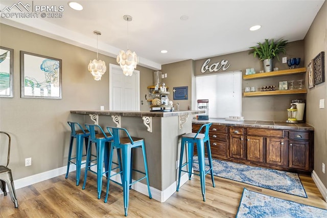 6950 Blue Mesa Ln, Littleton, CO 80125 - kitchen featuring a breakfast bar area, light wood-style flooring, open shelves, hanging light fixtures, and recessed lighting