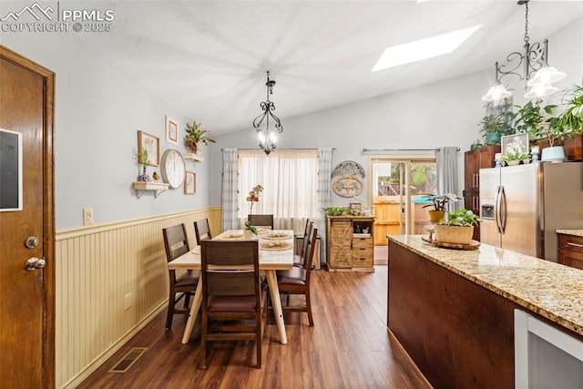 6150 Fall River Dr, Colorado Springs, CO 80918 - dining room featuring a skylight, vaulted ceiling, dark wood finished floors, a chandelier, and a wainscoted wall