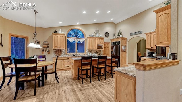 17910 Queensmere Dr, Monument, CO 80132 - kitchen featuring tasteful backsplash, stainless steel microwave, a kitchen bar, light wood finished floors, and light brown cabinets