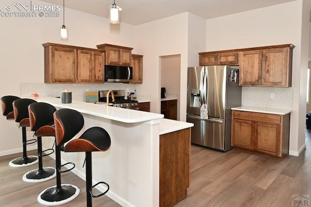 1213 E Tidy Dr, Pueblo, CO 81007 - kitchen featuring stainless steel appliances, brown cabinets, a peninsula, tasteful backsplash, and wood finished floors