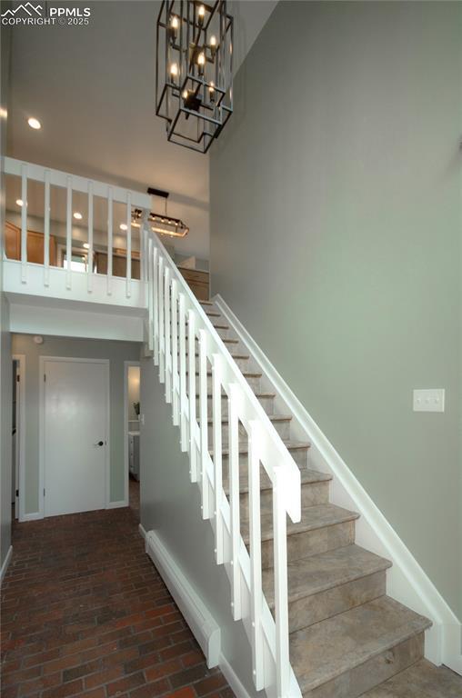 16070 Buggywhip Dr, Elbert, CO 80106 - stairway featuring brick flooring, a chandelier, a towering ceiling, baseboards, and recessed lighting