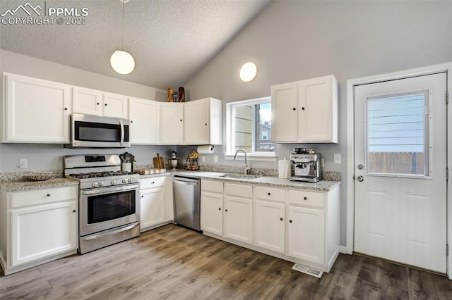 13072 Westlake Pl, Broomfield, CO 80020 - kitchen featuring appliances with stainless steel finishes, vaulted ceiling, a sink, white cabinets, and wood finished floors