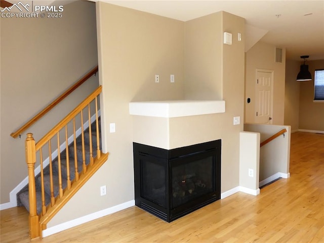 828 S Wahsatch Ave, Colorado Springs, CO 80903 - unfurnished living room featuring wood finished floors, baseboards, stairway, and a multi sided fireplace