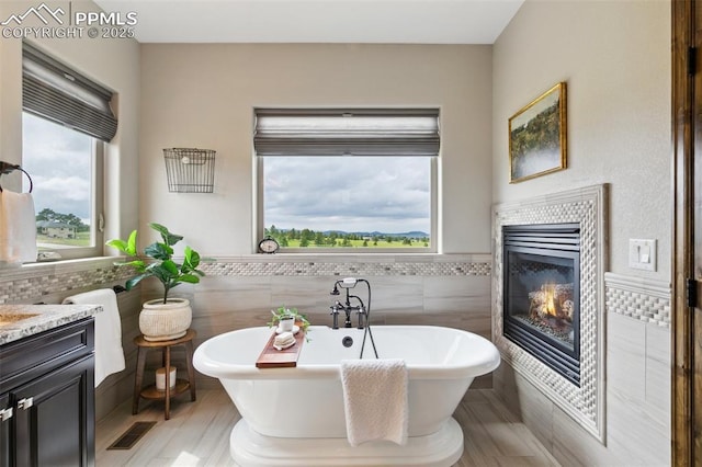 4808 Silver Nell Dr, Colorado Springs, CO 80908 - bathroom featuring tile walls, a soaking tub, vanity, a tile fireplace, and a wainscoted wall