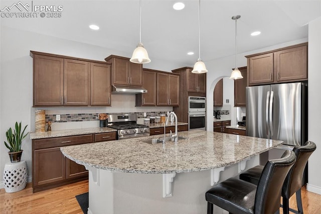 9661 Fresh Air Dr, Colorado Springs, CO 80924 - kitchen featuring appliances with stainless steel finishes, a sink, under cabinet range hood, arched walkways, and a kitchen bar
