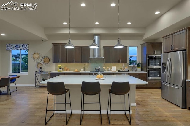 16277 Gammon Ct, Monument, CO 80132 - kitchen featuring appliances with stainless steel finishes, light countertops, dark brown cabinetry, backsplash, and wall chimney exhaust hood