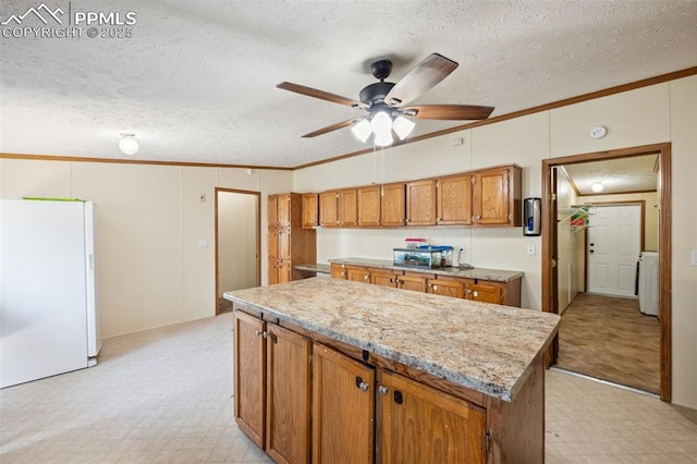842 Desert Cir, Fountain, CO 80817 - kitchen with freestanding refrigerator, light flooring, crown molding, brown cabinetry, and a textured ceiling