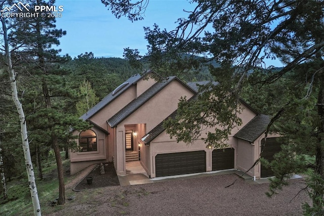 2100 N Elk Rdg, Divide, CO 80814 - view of front of property featuring stucco siding, an attached garage, driveway, and a forest view