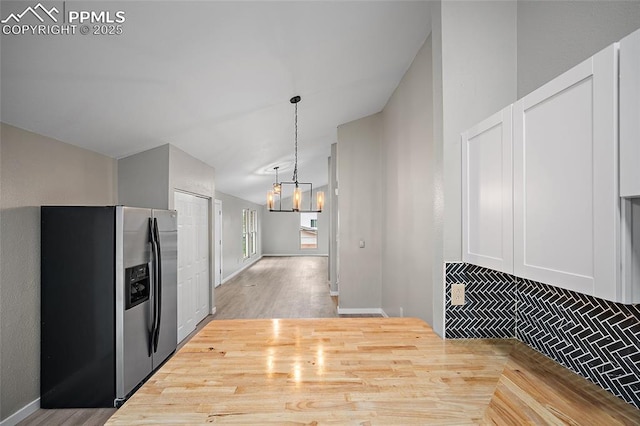 4408 Winding Cir, Colorado Springs, CO 80917 - kitchen with stainless steel fridge, a chandelier, vaulted ceiling, white cabinets, and hanging light fixtures
