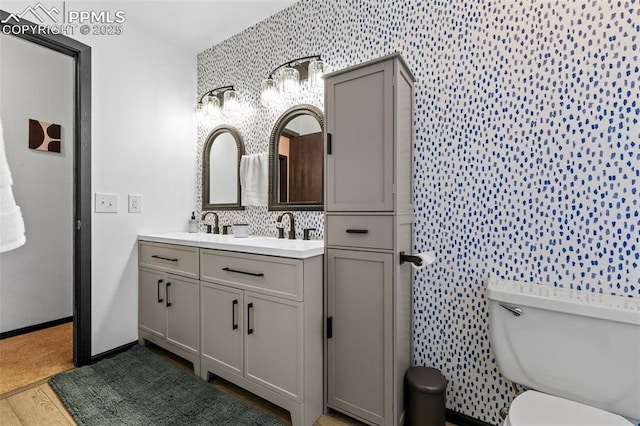 4303 W Eastcrest Cir, Colorado Springs, CO 80916 - full bath featuring wallpapered walls, double vanity, toilet, wood finished floors, and baseboards