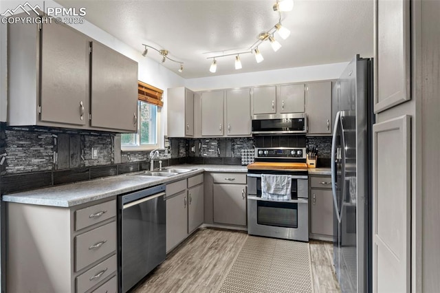 4303 W Eastcrest Cir, Colorado Springs, CO 80916 - kitchen with appliances with stainless steel finishes, gray cabinetry, a sink, tasteful backsplash, and light wood finished floors