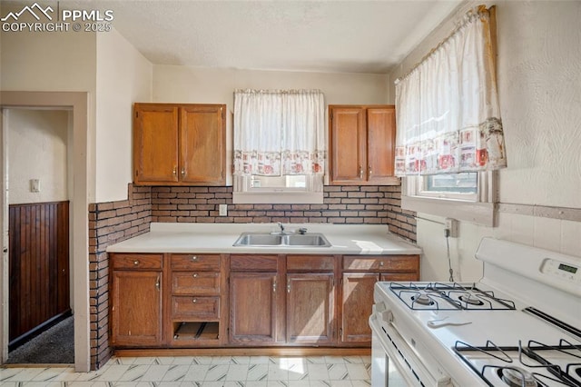 117 S Limit St, Colorado Springs, CO 80905 - kitchen featuring white range with gas cooktop, a sink, light countertops, brown cabinetry, and wainscoting